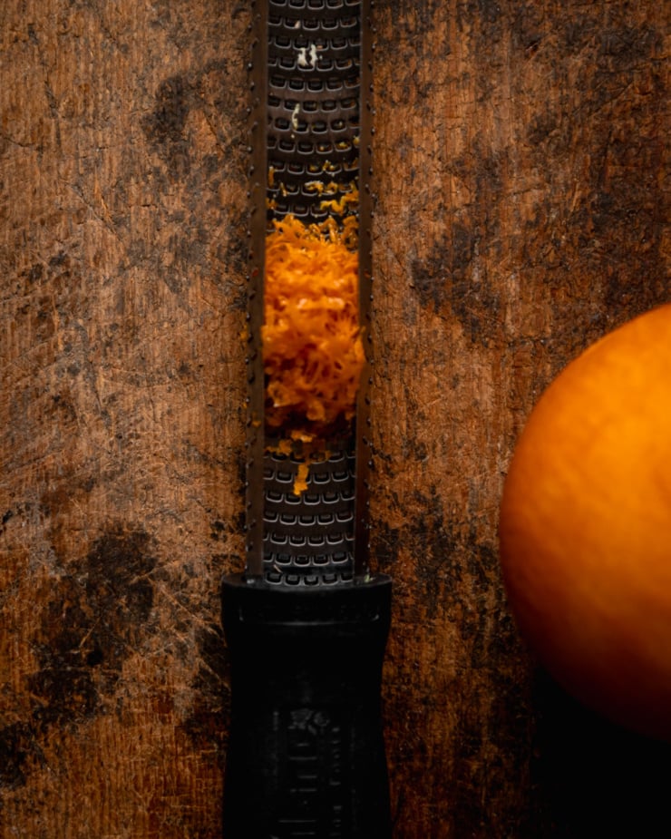 An overhead shot shows orange zest collected in a Microplane. An orange is nearby.