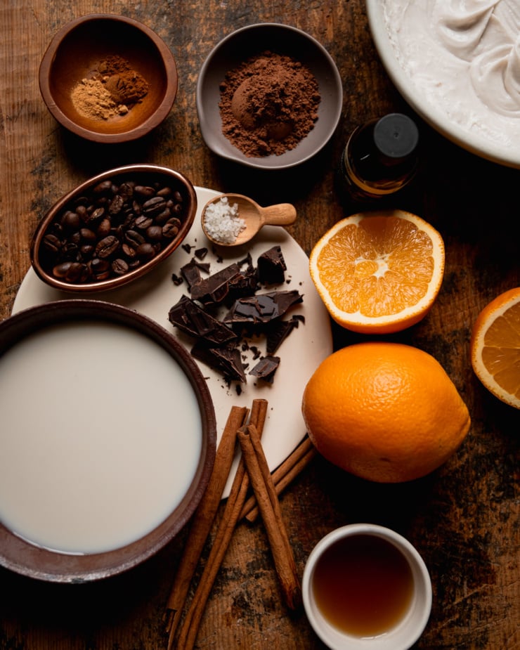 An overhead shot shows ingredients for a vegan orange mocha coffee drink, all on a rough wood background.