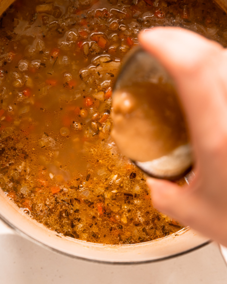 An overhead shot shows a hand pouring a bowl of miso and vegetable stock into a pot of soup.