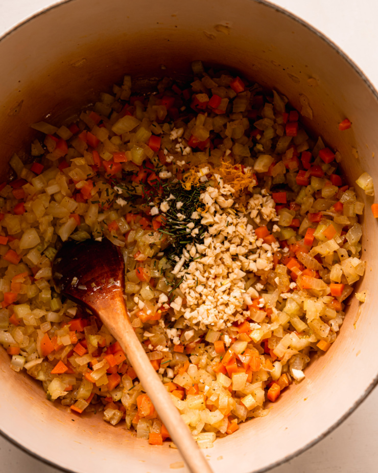An overhead shot shows sautéed vegetables in a pot. Minced garlic, rosemary, and lemon zest have just been added.