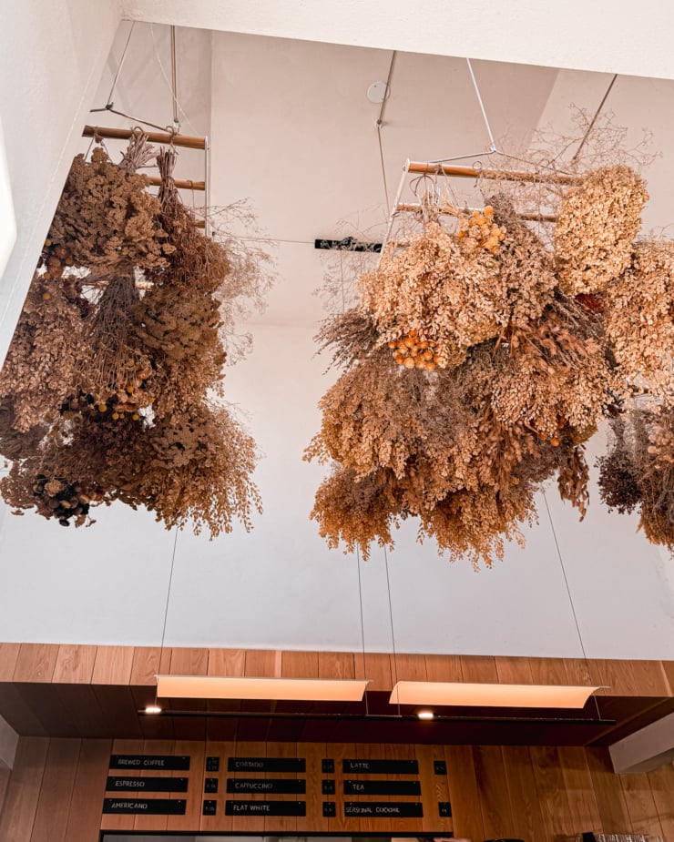 An upward angled image shows dried flowers hanging from the ceiling in a café