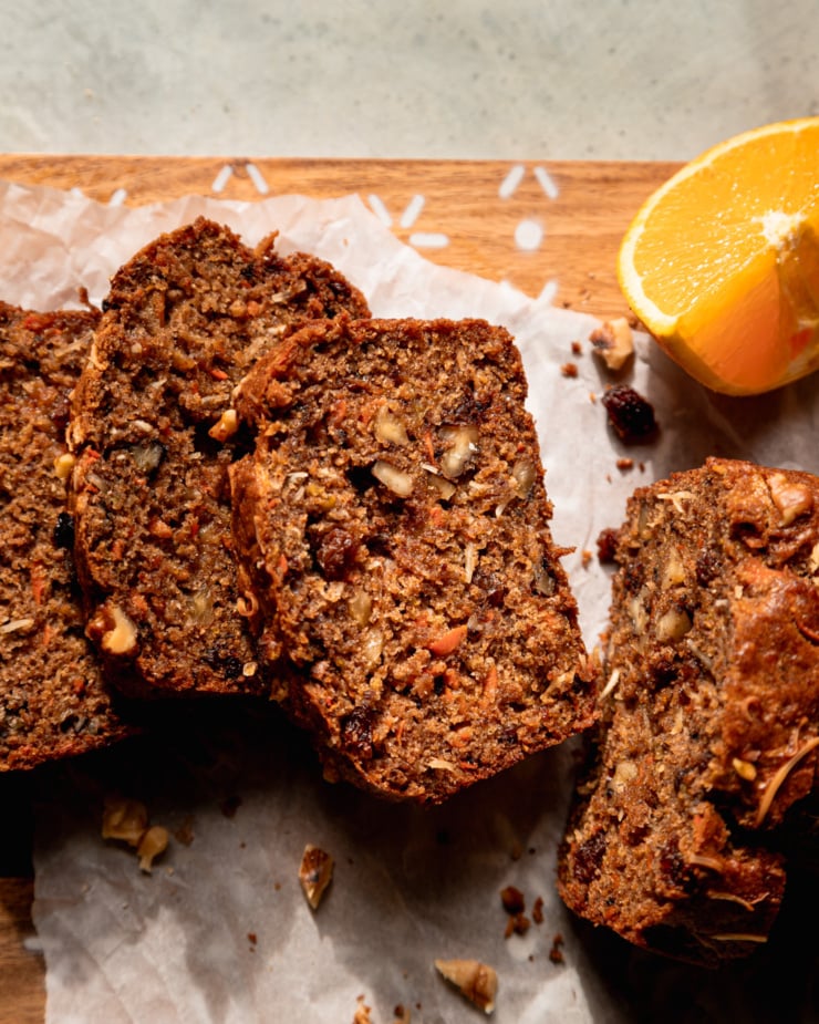 An overhead shot shows slices of a vegan morning glory bread. A wedge of fresh orange is nearby.