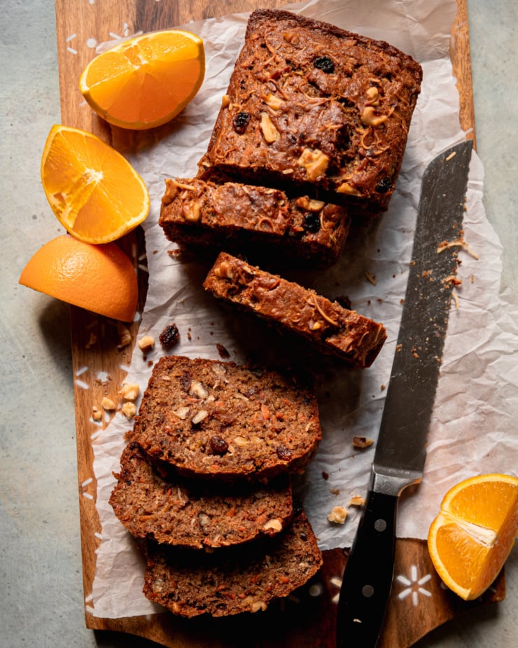 An overhead shot shows a sliced morning glory bread on a parchment-lined cutting board. Orange slices are seen nearby.