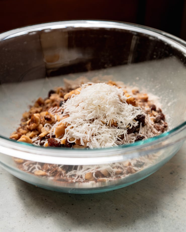 A head-on shot shows a bowl filled with dry ingredients like flour, cinnamon, walnuts, raisins, and coconut.