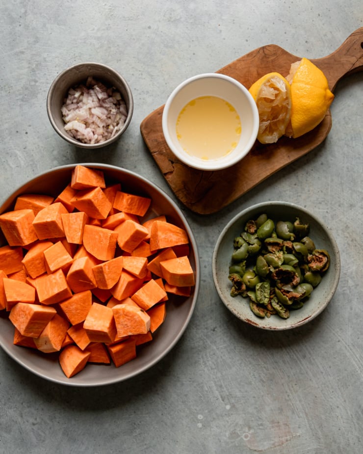 An overhead shot shows chopped sweet potatoes, a juiced lemon, chopped Castelvetrano olives, and minced shallots.