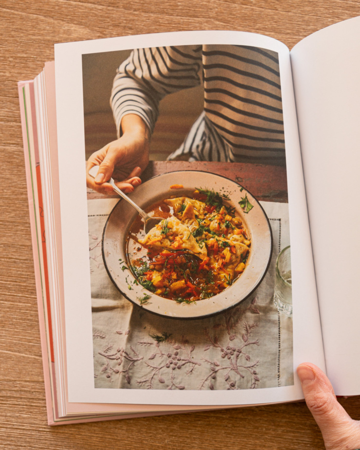 An overhead shot shows a photo from the cookbook "Kapusta" depicting a bowl of vegetable dumplings on a tablecloth-lined table.