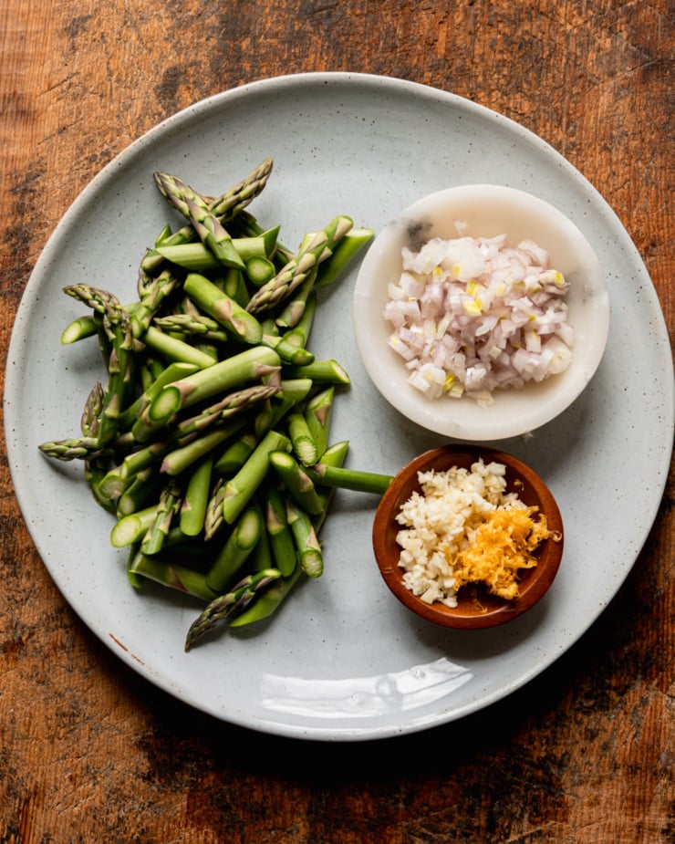 An overhead shot shows a plate with chopped asparagus, diced shallots, minced garlic, and lemon zest.