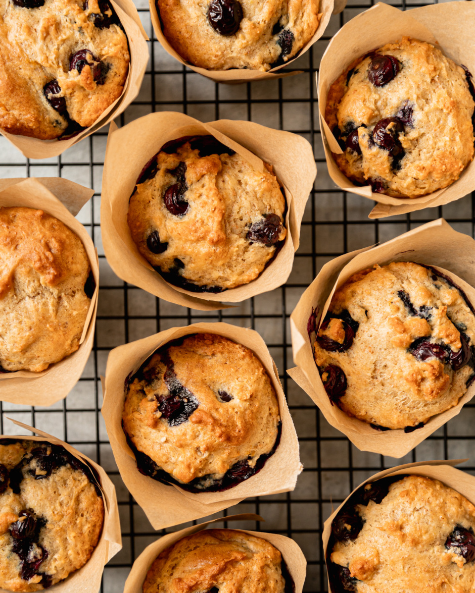 An overhead shot shows vegan blueberry muffins cooling on a wire rack. The muffins are wrapped in homemade parchment muffin liners.