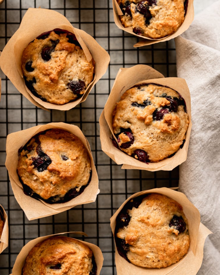 An overhead shot shows fluffy vegan blueberry muffins cooling on a wire rack. The muffins are in homemade parchment paper liners.