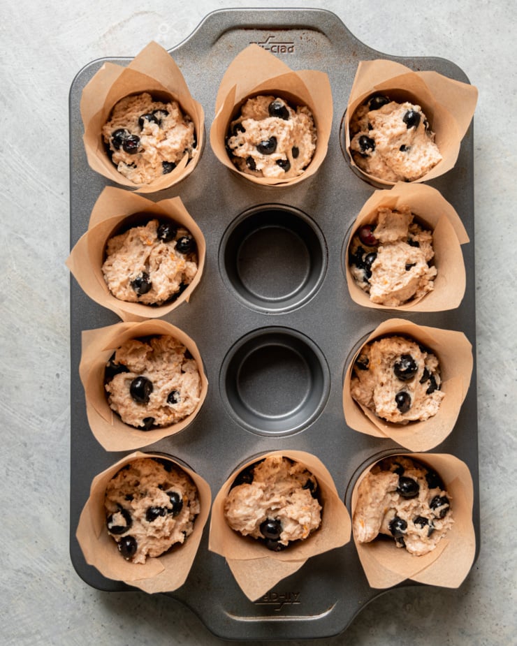 An overhead shot shows blueberry muffin batter portioned into homemade muffin cups in a muffin tin.