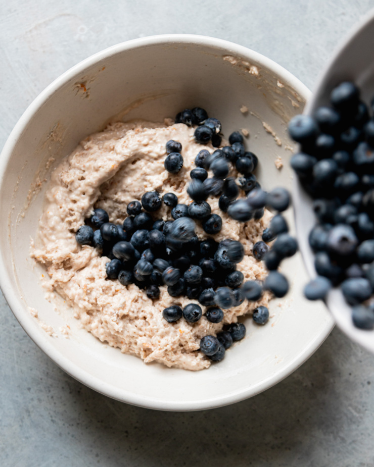 An overhead shot shows fresh blueberries being poured into a bowl of batter.