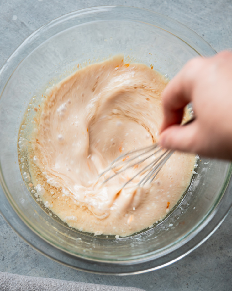 An overhead shot shows a hand using a whisk to bring wet ingredients together in a bowl.