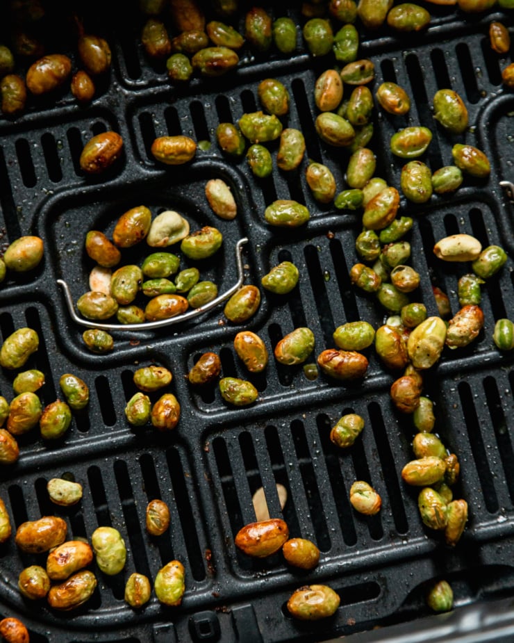 An up close, overhead shot shows edamame browning in an air fryer basket.