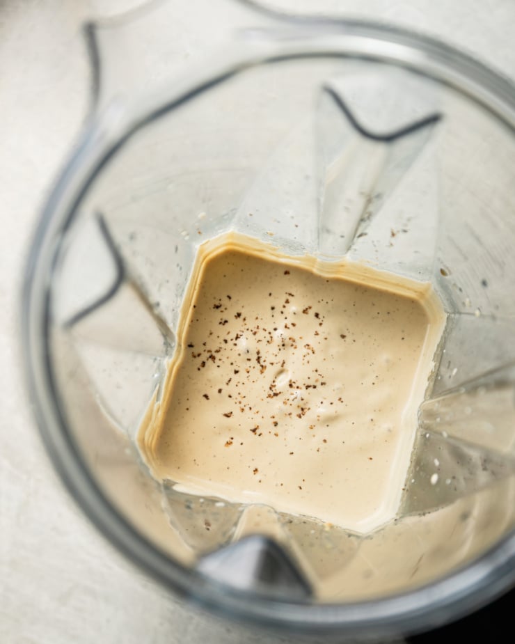 An overhead shot shows a creamy vegan Caesar dressing in the pitcher of a blender.