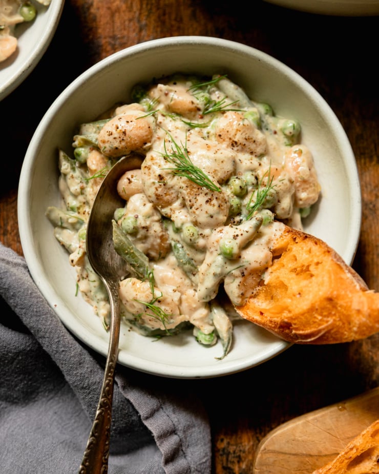 An overhead shot shows a serving bowl of dilly beans and peas with a piece of crusty bread sticking out.