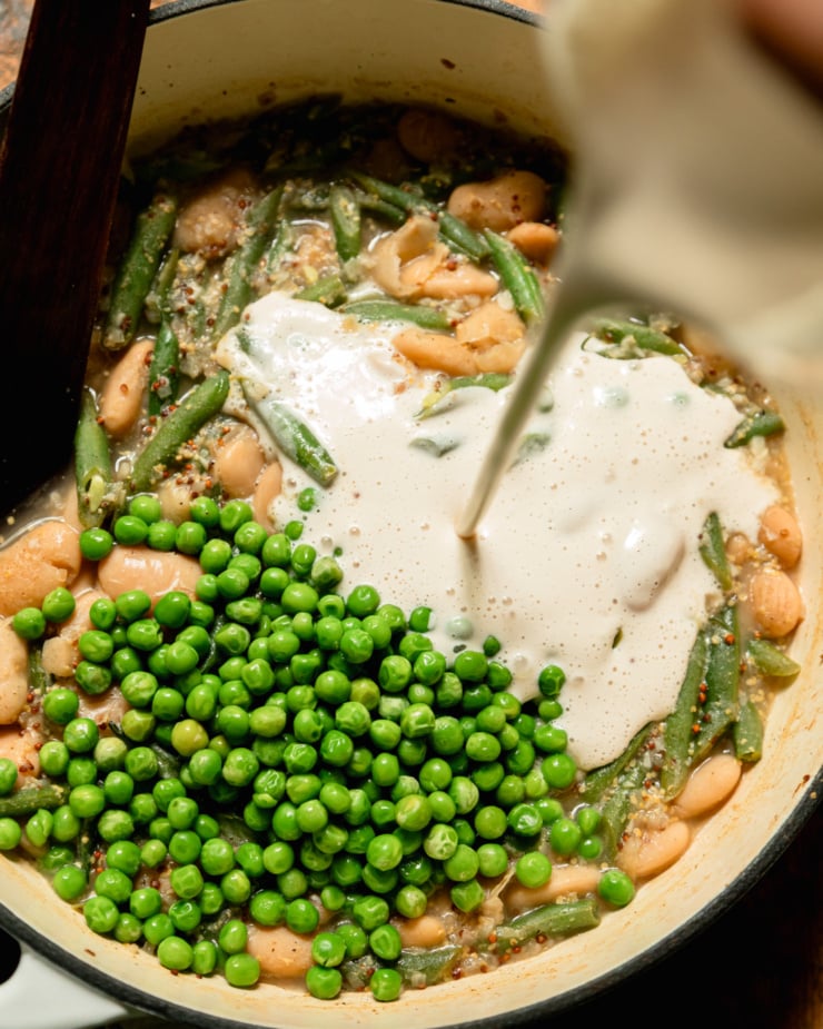 An overhead shot shows cashew cream being poured into a pot with butter beans, green beans, peas, and vegetable stock.