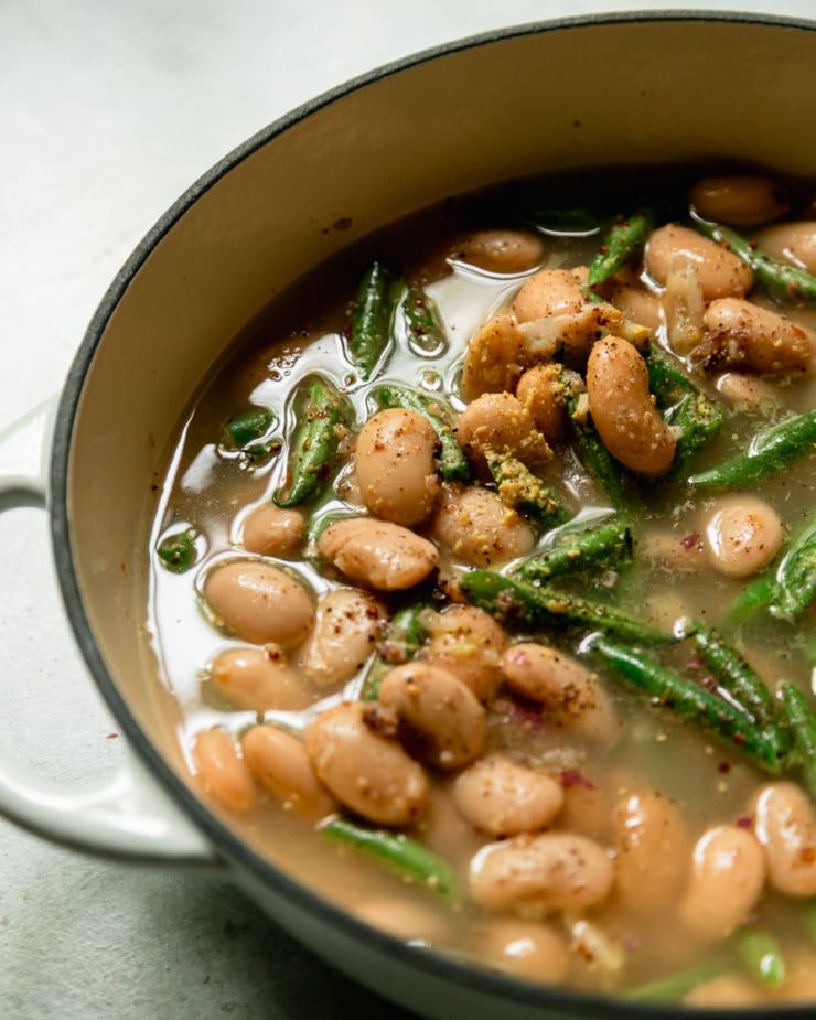 A 3/4 angle shot shows butter beans, green beans and vegetable stock in a braiser.