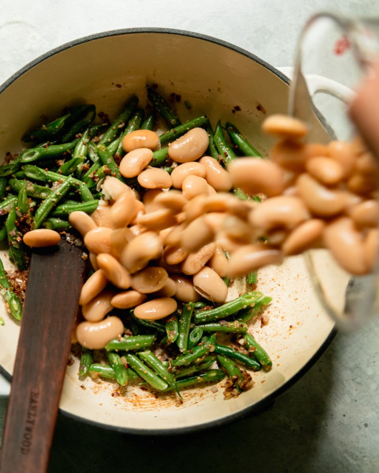 An overhead shot shows butter beans being poured into a skillet with some sautéed green beans.
