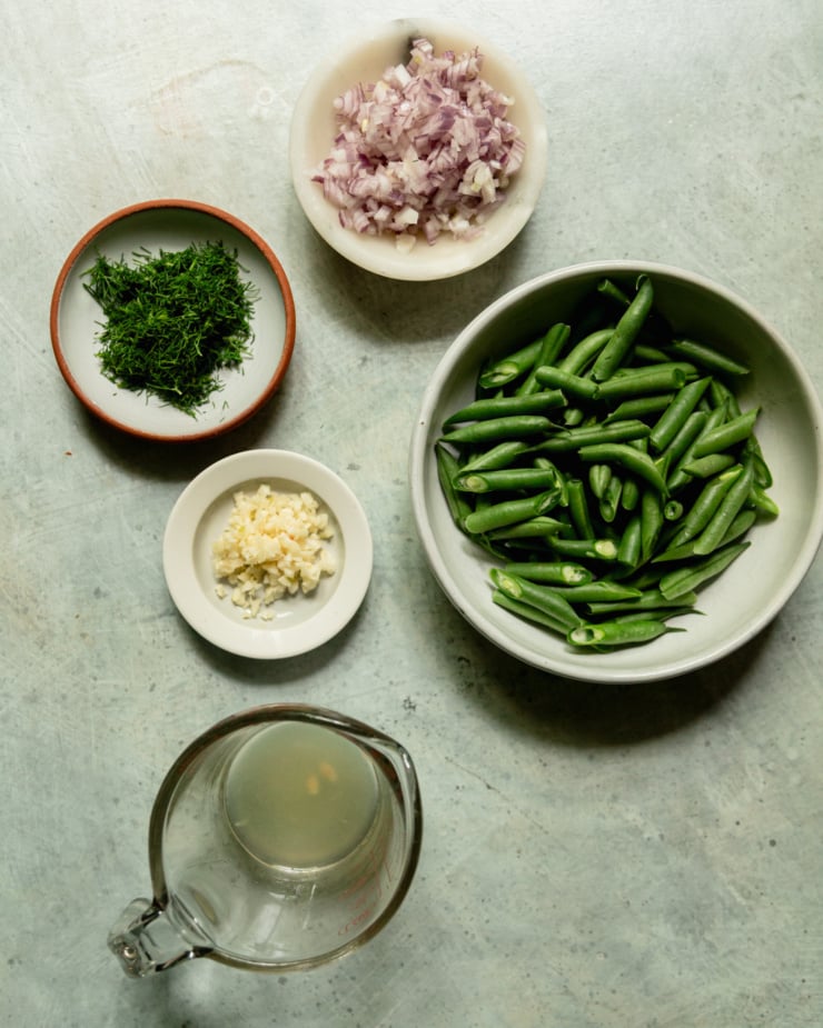 An overhead shot shows bowls of diced shallot, cut green beans, lemon juice, minced garlic, and chopped dill.