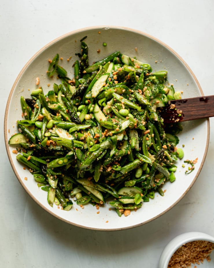 An overhead shot shows a wide bowl filled with a roasted asparagus salad that also features snap peas, cucumber, edamame, fresh mint, and finely chopped peanuts.