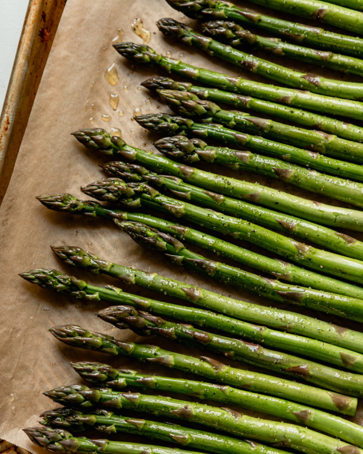 An overhead shot shows asparagus spears on a baking sheet.