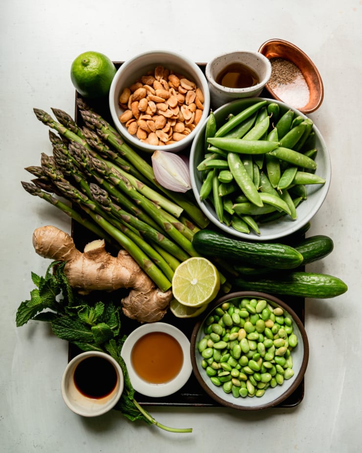 An overhead shot shows ingredients for a roasted asparagus salad with snap peas, cucumber, peanuts, and ginger lime dressing.