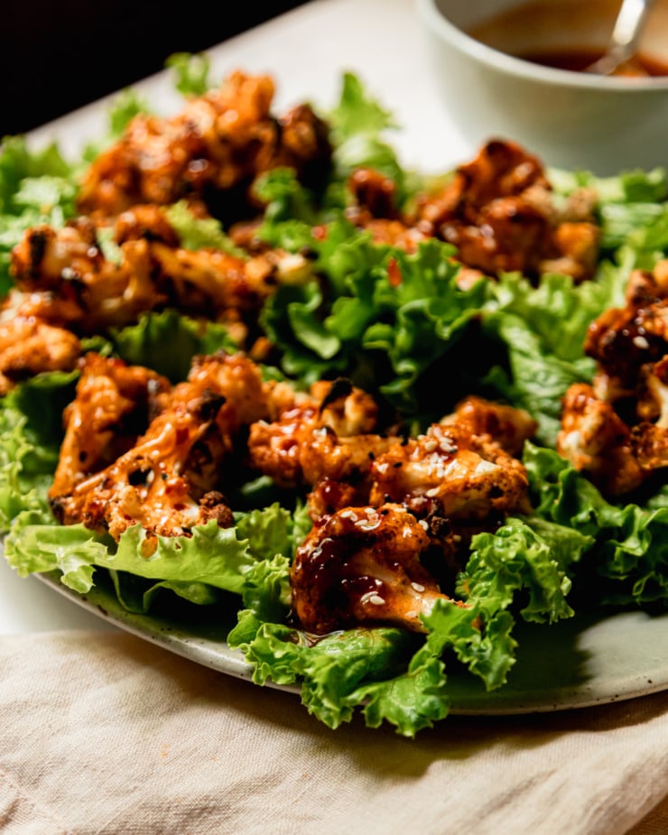A head-on shot shows a latter of roasted cauliflower lettuce wraps that have been liberally drizzled with homemade sweet chili sauce.