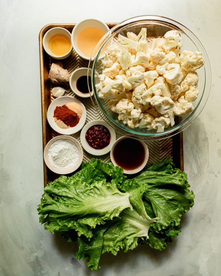 An overhead shot shows ingredients needed for roasted cauliflower lettuce wraps with sweet chili sauce, all prepped and measured out on a baking sheet.