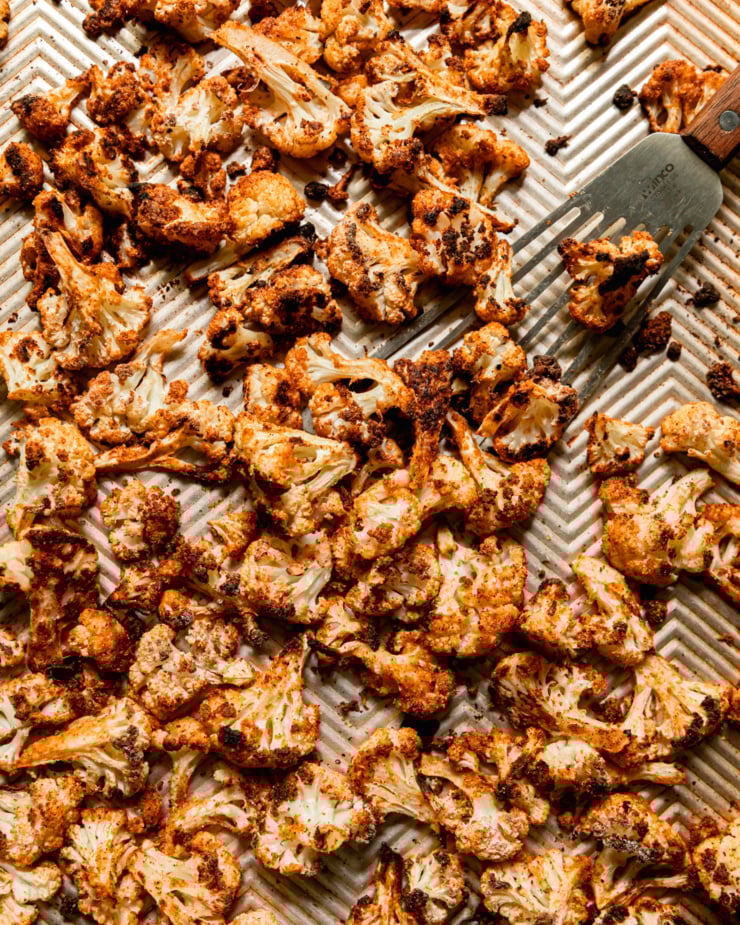 An up close, overhead shot shows deeply caramelized and spice-crusted florets of cauliflower on a baking sheet.