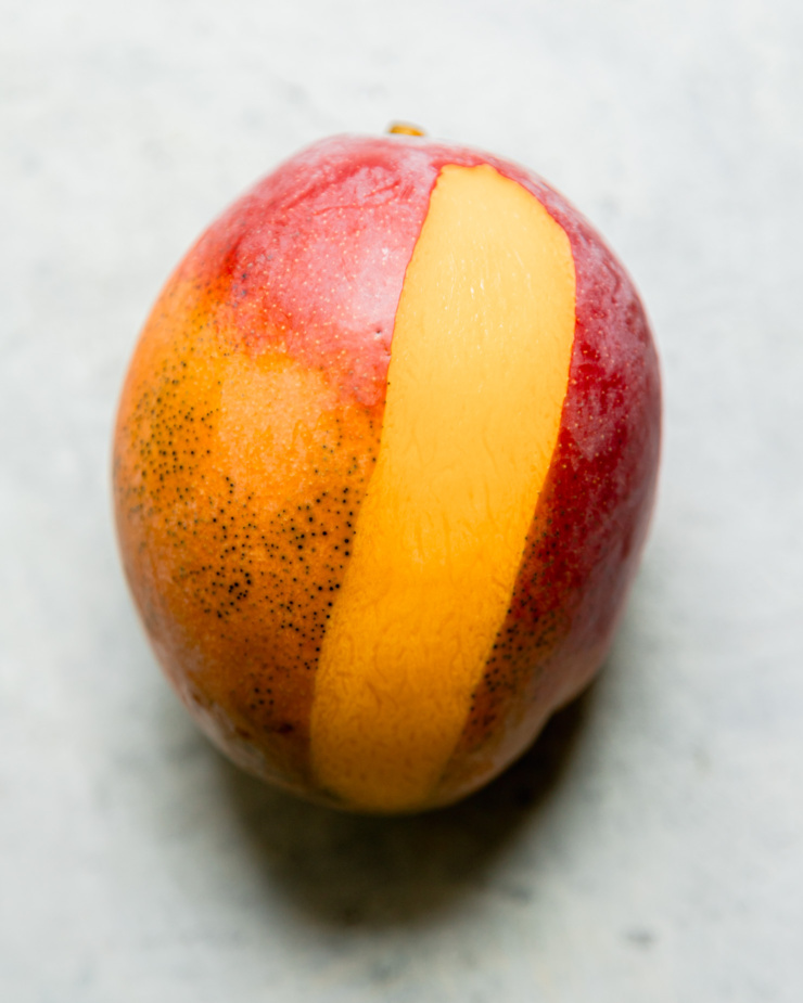 An overhead shot shows a mango with one strip of peel removed.