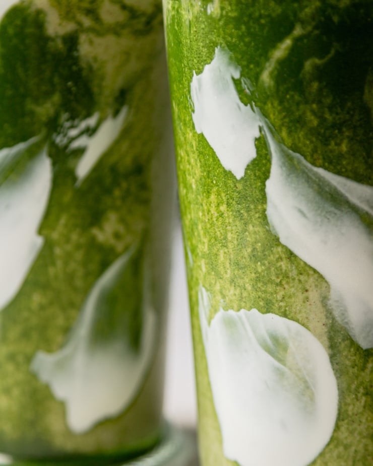 An up close shot shows two glasses of matcha smoothie almost layered on each other. Through the glass you can see swirls of light green, dark green and white.