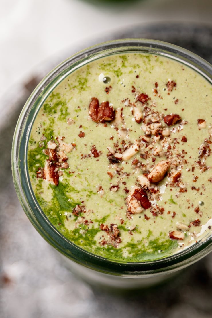 An overhead shot shows a matcha banana smoothie garnished with crushed toasted pecans.