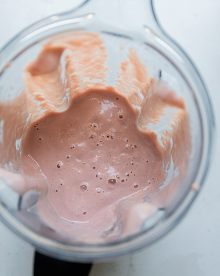 An overhead shot shows a rich rhubarb strawberry cashew milk mixture in a Vitamix blender jar