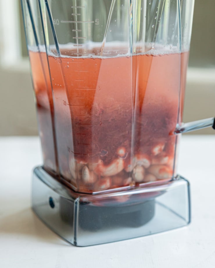 A head-on shot shows a blender jar containing raw soaked cashews, water, and a rhubarb strawberry compote. This is prior to blending it up into a "cream" of sorts.