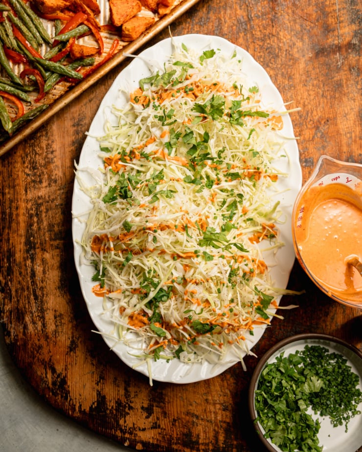 An overhead shot shows a platter of shredded cabbage and chopped herbs drizzled with peanut Gochujang dressing.
