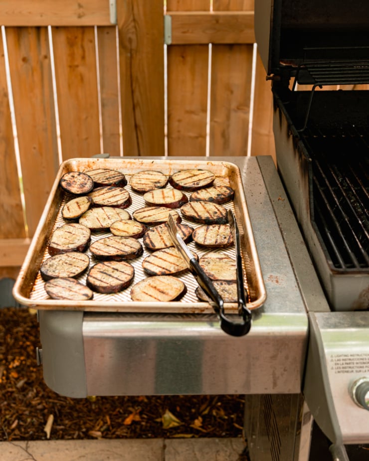 A head-on shot shows a tray of grilled Japanese sweet potatoes on the little side table of a BBQ grill.