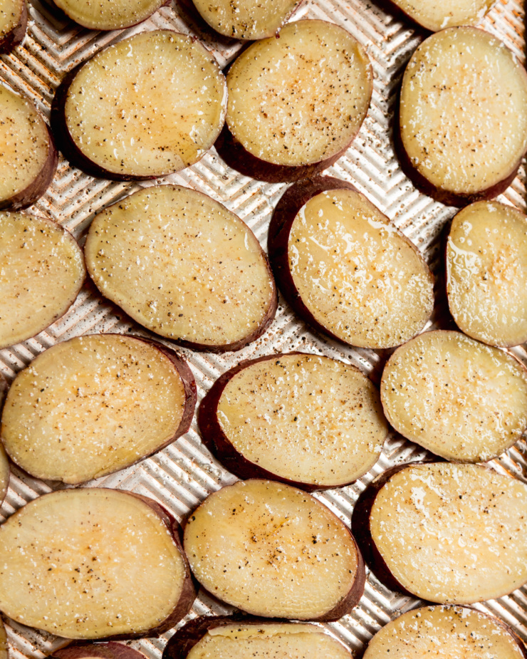An overhead shot shows potato slices slicked with olive oil and seasoned with salt and pepper.