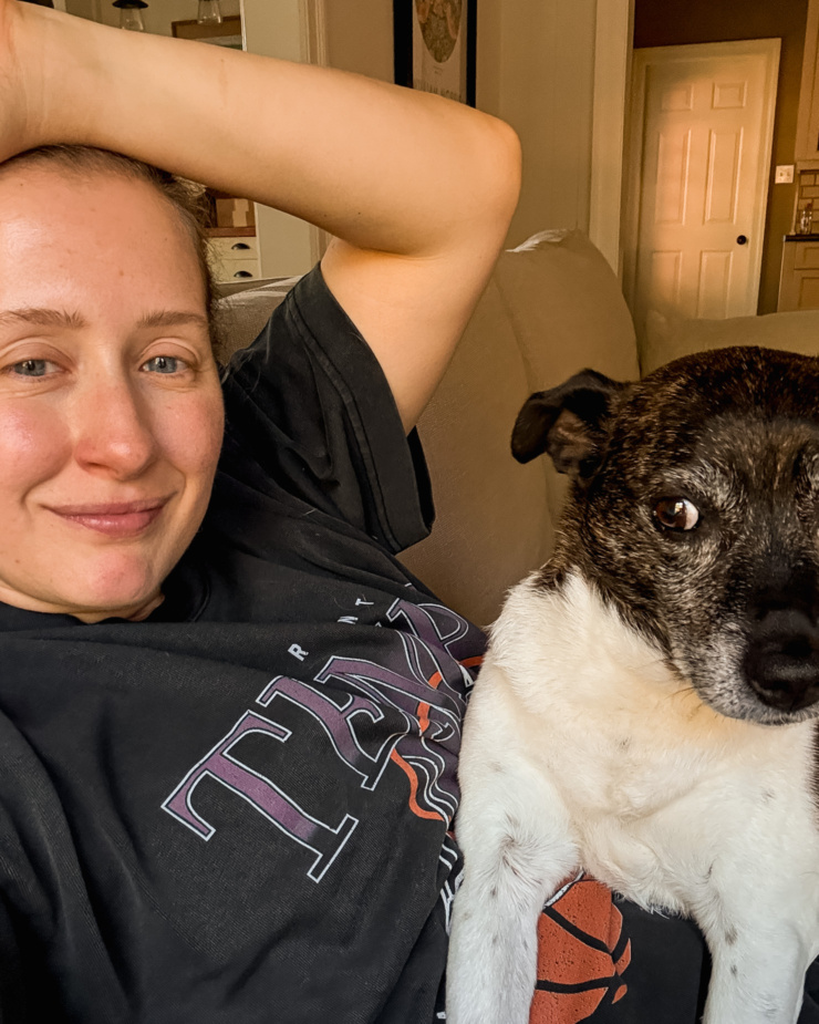 A selfie shot shows a woman sitting with her dog on the couch.