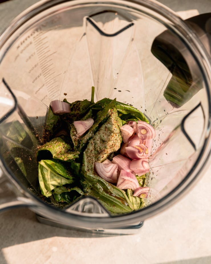 An overhead shot shows diced shallots and basil leaves in a blender pitcher.
