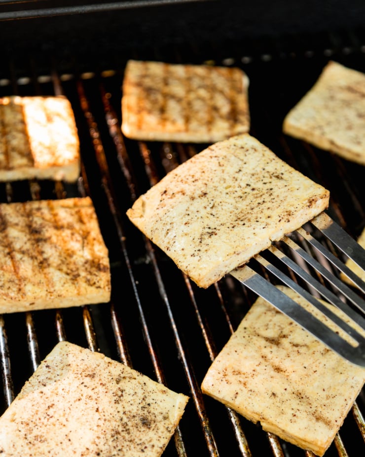 A 3/4 angle shot shows tofu slices on an outdoor grill.