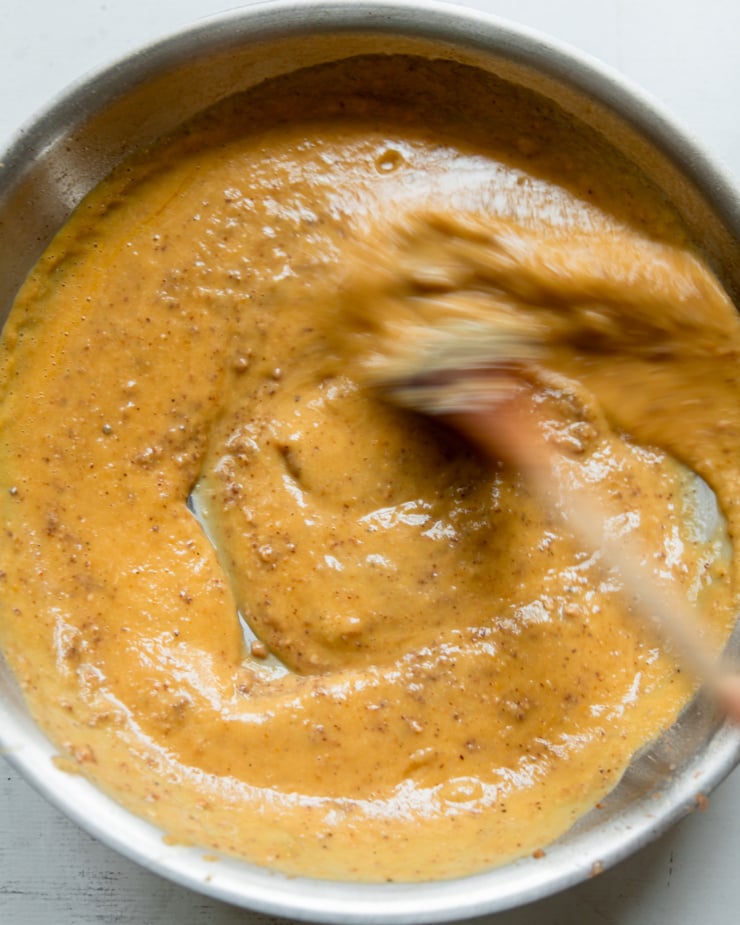 An overhead shot shows a peach, almond butter and miso sauce in a pan that is being stirred by a spoon.