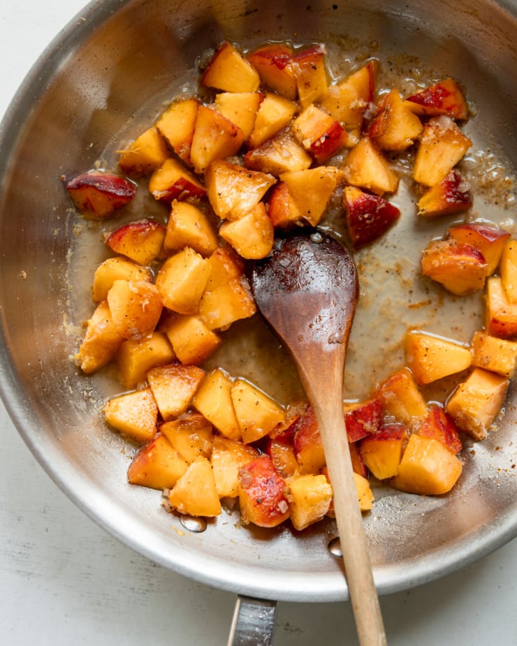An overhead shot shows diced peaches sautéing in a pan with a wooden spoon.