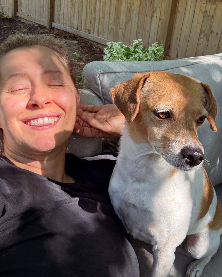 A selfie shows a woman and her chihuahua whippet mixed dog sitting in the sunlight.