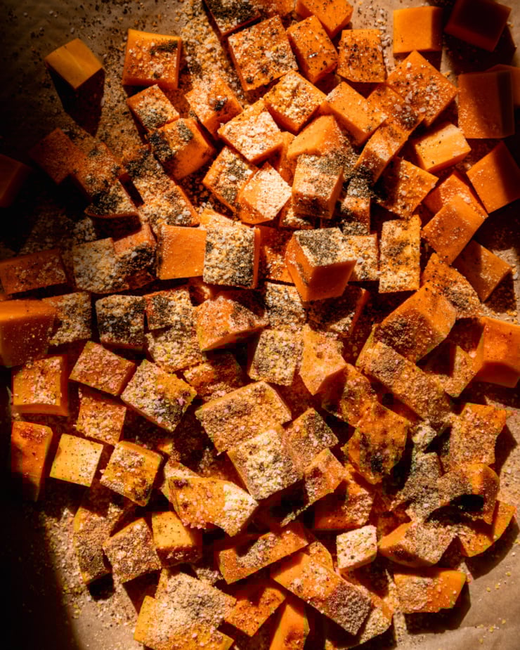 An overhead shot shows cubed raw squash dusted with spices.