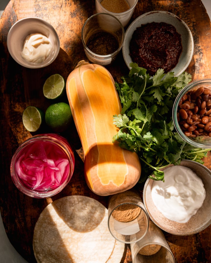 An overhead shot shows ingredients for vegan butternut squash tacos on a wood board.
