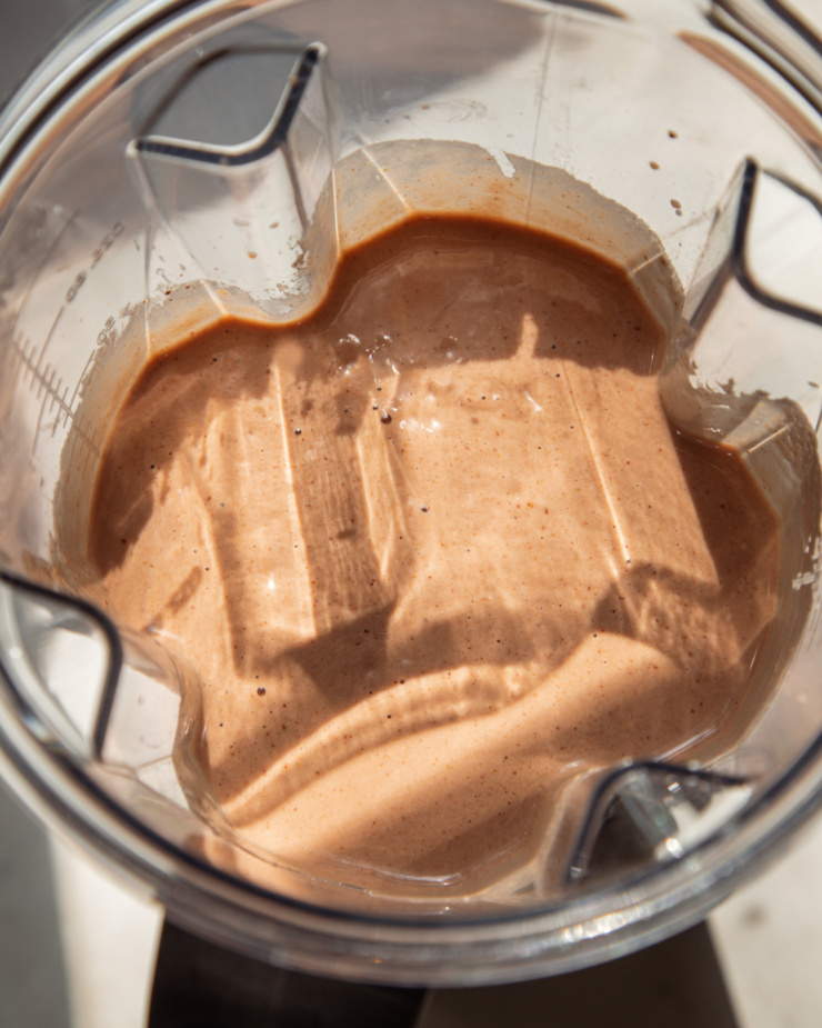 An up close, overhead shot shows a chocolate pear smoothie, freshly blended, in a Vitamix blender jug in bright sun light.
