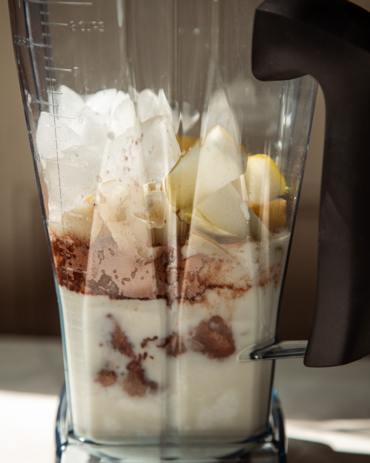 A head-on shot shows a blender pitcher filled with ingredients to make a smoothie.