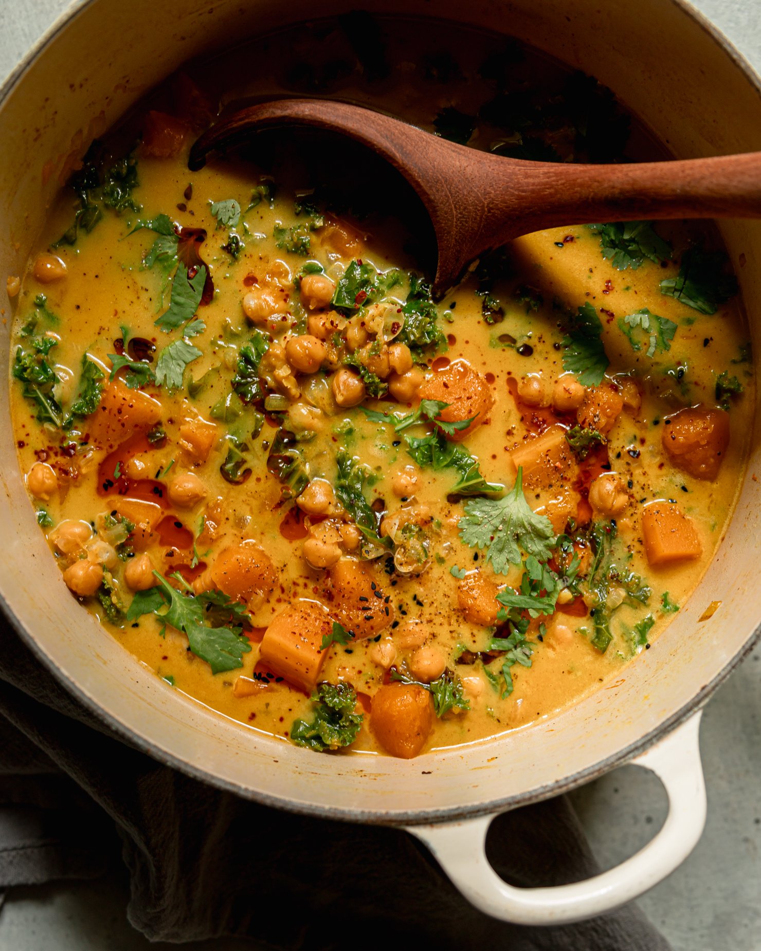 An overhead shot shows a pot of butternut squash stew. A wooden ladle is sticking out of the pot. The broth appears creamy and golden.