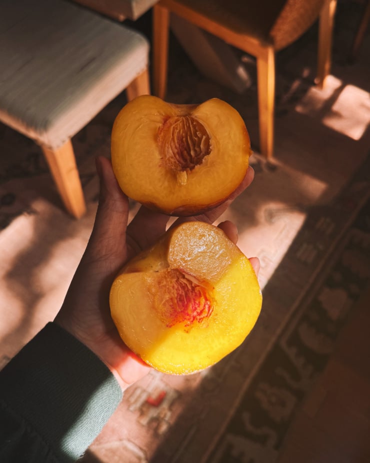 An overhead shot shows a hand holding two giant halves of a very juicy peach.