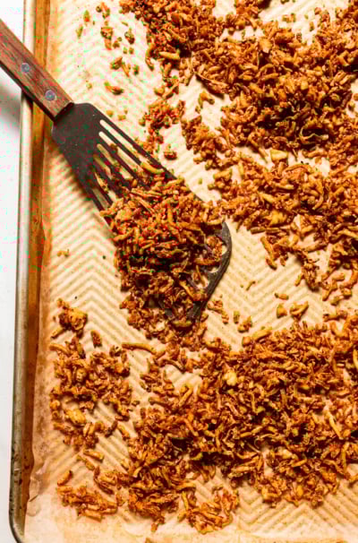 An overhead shot shows a baking sheet filled with crispy and chewy baked shredded tofu. A metal spatula is seen to the side.